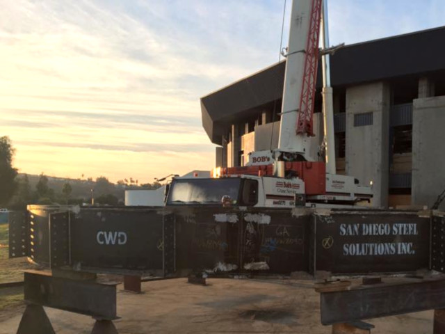 Picture of a crane and large steel beams marked with San Diego Steel Solutions, Inc. and another with C.W.D.